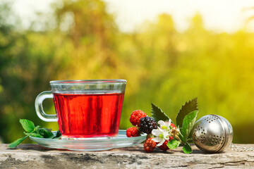 Blackberry tea with some berries and mint leaves and tea strainer over an old wood with green...