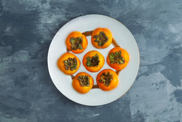 Sliced Persimmon fruit in a metal dish with grey and  blue background. Top view