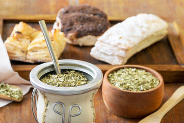 Yerba Mate drink over a wooden table with pastries and a bowl with yerba mate sticked dried leaves