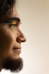 portrait of a gay hispanic man in makeup with a rainbow in his eyes on a white background smiling