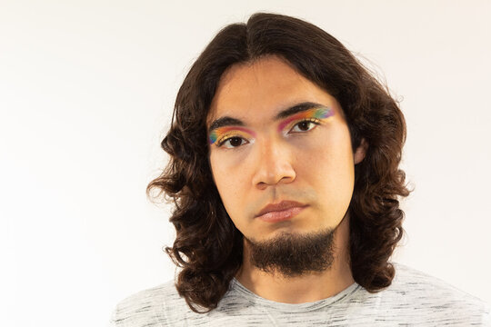 Portrait Of A Gay Man Made Up With A Rainbow In His Eyes On A White Background With A Serious Face