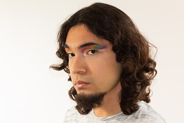 portrait of a gay man made up with a rainbow in his eyes on a white background with a serious face