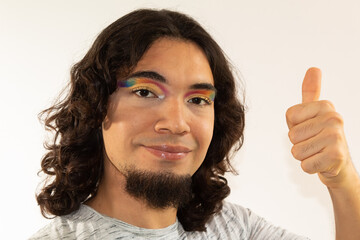 portrait of a gay hispanic man in makeup with a rainbow in his eyes on a white background smiling