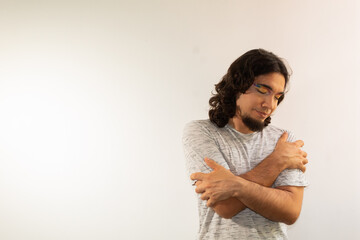 portrait of a gay man made up with a rainbow hugging himself on a white background