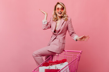 Pretty woman is sitting in beautiful jacket and pants on pink trolley and spreads her arms to side