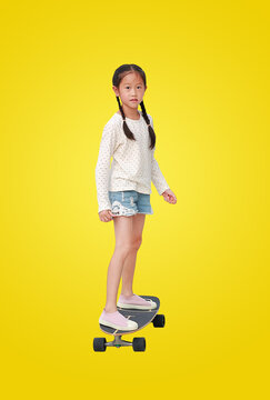 Asian little girl child skating on a skateboard isolated on yellow background. Kid riding on skateboard. Image with Clipping path