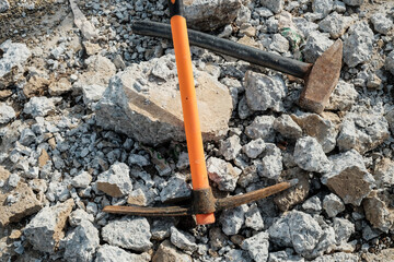 Geological pick with orange handle on the stones next to old hammer