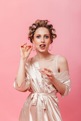 Blue-eyed housewife in bathrobe eats olive and holds martini glass on pink background