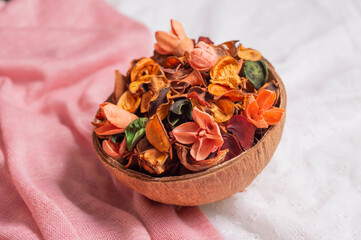 A coconut bowl with dried flowers and petals of buds on a pink and white fabric.