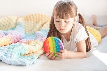 little cheerful girl plays in a multi-colored plastic toy pop it while lying on the bed. playing at home during summer holidays