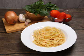 Cooked spaghetti on white plate with ingredients roma tomato glass bowl basil onion garlic wooden board recipe on table marble wall