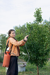 women farmer spraying fertilizers and trace elements with portable sprayer on trees in garden to...
