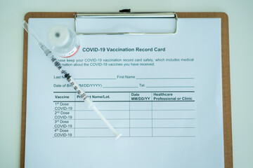 COVID-19 or coronavirus vaccine in a bottle and needle with the COVID-19 vaccination record document.