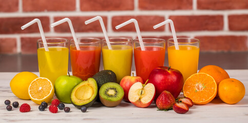 Different fruits juice in glass, apple, orange and strawberry juice with straw, looking refreshing on colourful wood board in front of brick wall background. Picture decorating with fresh fruits