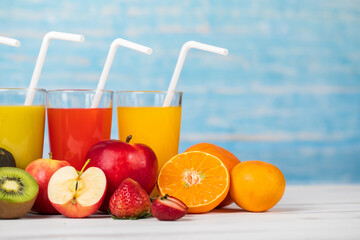 Different fruits juice in glass, apple, orange and strawberry juice with straw, looking refreshing on colourful wood board in front of blue wall background. Picture decorating with fresh fruits