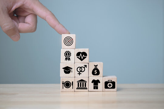 Human hand point cube wood with icons, education, health, housing, gender, basic human needs concept.