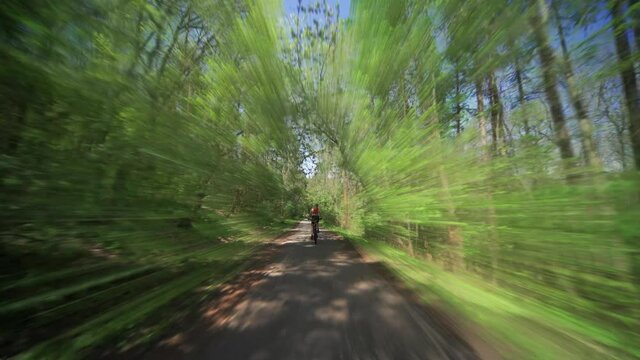 A solo female cyclist riding on the narrow forest road in the natural reserve of the Divoka Sarka in Prague.