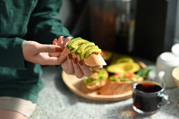 Woman sitting in kitchen and eating avocado sandwiches.