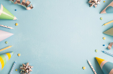 Birthday party background. Carnival caps, confetti, streamers and candles on pastel blue surface....