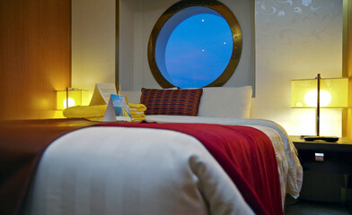 Bedroom of oceanview suite cabin stateroomwith large porthole window  in clean modern cozy interior...