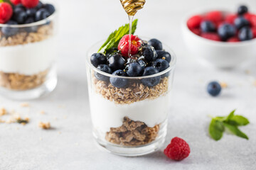 Honey is poured on granola with yogurt, blueberries and raspberries. Healthy breakfast. Menu, recipe.