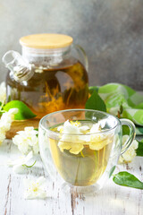 Therapeutic herbal tea. Hot Jasmine tea with jasmine flowers in a glass teapot on a rustic wooden table.