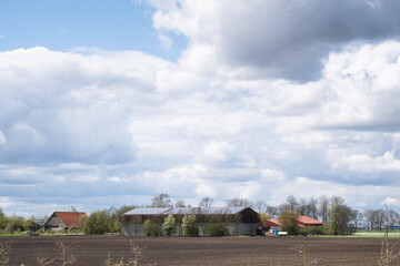 Farm with house and modern dairy barn in the flat landscape with plowed fields of the Noordoostpolder, the Netherlands. There are solar panels on the roof of the barn. Sustainable energy