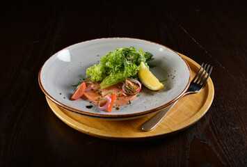 smoked salmon fish with vegetables, lemon and salad dressing appetiser in dark background western halal menu