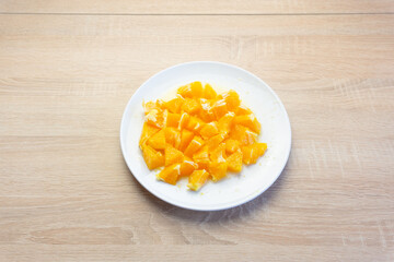 Orange cut into pieces in a white plate on a wooden table