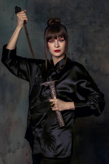 Beautiful woman with bright make up posing in Chinese costume in minimalistic interior with fan and dagger