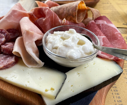 Rustic wooden serving tray with typical products of Italian Emilia-Romagna region:  Squacquerone and sliced cheese, Prosciutto (Ham), Salami, Coppa di testa, ciccioli. Brisighella, Italy