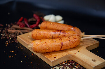 Raw sausage BBQ meat on bamboo skewers with vegetables and spices on black background. Free space...