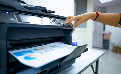 Office worker prints paper on multifunction laser printer. Copy, print, scan, and fax machine in...