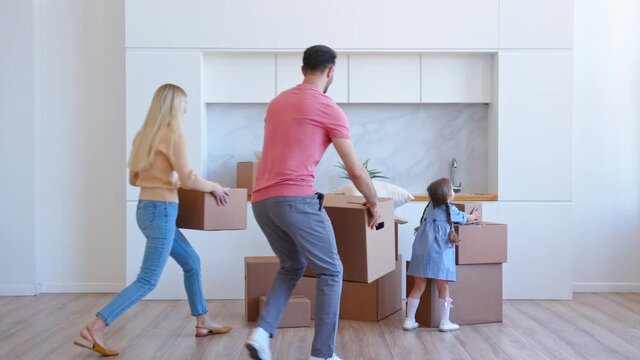 Joyful family with girl carries boxes into new apartment
