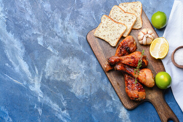 Board with roasted chicken legs on color background
