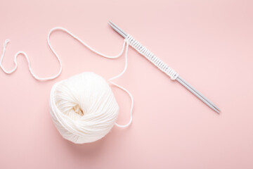 White knitting wool and knitting needles on pastel pink background. Hobby knitting. Top view