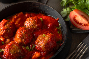Close up of stewed meatballs in tomato sauce in frying pan.