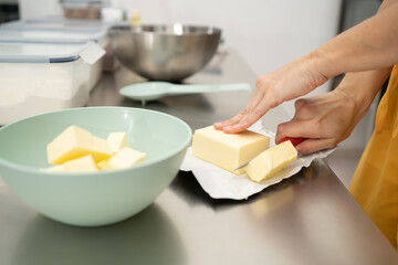 hands cutting butter with a red knife in a kitchen with unfocused background utensils. Concept of cooking, pastry.