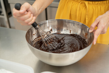 hands beating a chocolate mixture for a brownie in a metal bowl.