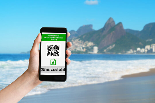 Hand holding mobile phone at Ipanema beach with international vaccination certificate on display