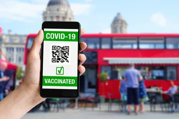 Rolgordijnen Hand met mobiele telefoon met covid-19 gevaccineerd op scherm en rode bus in Londen © Daniel Ernst