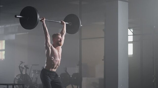 Slow motion of crossfit athlete performs clean and jerk. Young man doing the clean and jerk weightlifting exercise at the gym.
