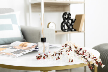 Blooming spring branches, reed diffuser and magazine on table in room