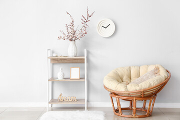 Vase with beautiful blossoming branches on shelving unit and armchair in room