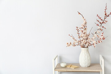 Vase with beautiful blossoming branches on shelving unit in room