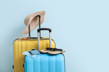 Packed suitcases with immune passport, medical masks and beach accessories on color background