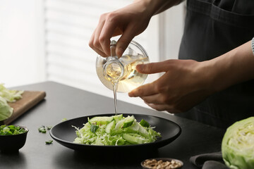Female chef cooking tasty cabbage salad on table in kitchen, closeup