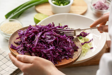 Female chef cooking tasty cabbage salad on table in kitchen, closeup
