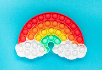 Multicolored silicone toy antistress pop it in the shape of a rainbow with clouds on a blue background - obrazy, fototapety, plakaty