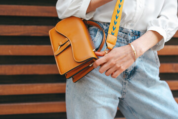 Fashion photo of woman wearing white shirt, jeans and brown crossbody bag against wooden background